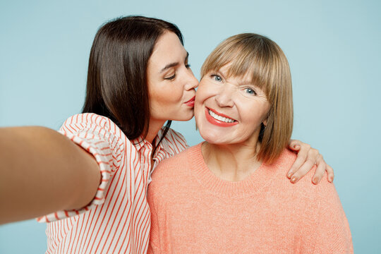 Close up elder parent mom with young adult daughter two women together in casual clothes doing selfie shot pov on mobile cell phone kiss hug isolated on plain blue cyan background Family day concept
