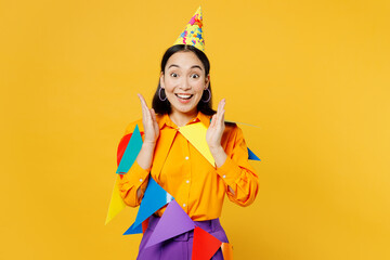 Happy fun surprised shocked young woman wears casual clothes hat celebrating wrapped in bunting flags spread hands look camera isolated on plain yellow background. Birthday 8 14 holiday party concept.