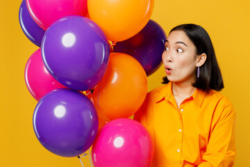 Fototapeta na wymiar Close up happy fun surprised young woman wearing casual clothes celebrating holding looking at bunch of colorful air balloons isolated on plain yellow background. Birthday 8 14 holiday party concept.