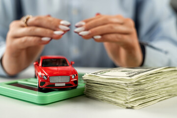Car on US dollar bills and calculator on glass table with hands over car.