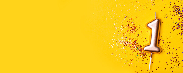 Gold candle in the form of number one on yellow background with confetti.
