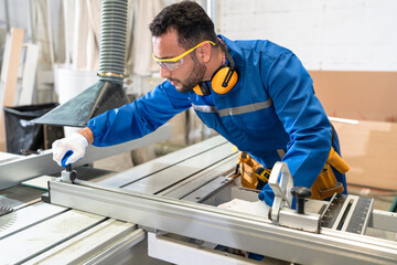 Handsome carpenter in safety uniform checking machine at wood factory	