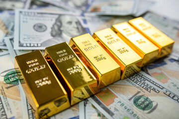 closeup gold bar lying on 100 dollar bills