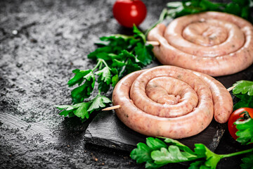 Raw sausages on a stone board with parsley and tomatoes. 
