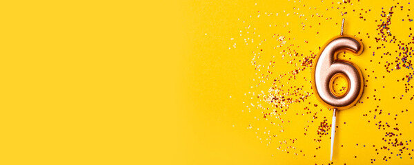 Gold candle in the form of number six on yellow background with confetti.