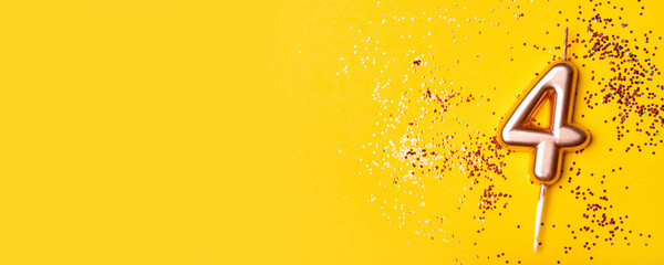 Gold candle in the form of number four on yellow background with confetti.