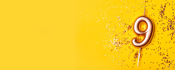 Gold candle in the form of number nine on yellow background with confetti.