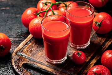 Tomato juice in glasses on a wooden cutting board. 