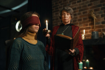 Old mature gypsy fortune teller reading witchcraft spell from book for woman