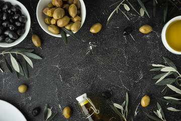 Green and black olives in white bowls next to a bottle with olive oil and leaves on a black background. .Bottle of cold pressed oil. Traditional Greek and Italian food. Flat lay. Copy space