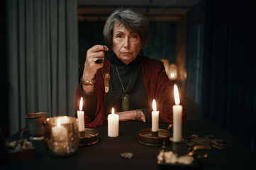 Portrait of fortune teller holding crystal pendant for divination seance