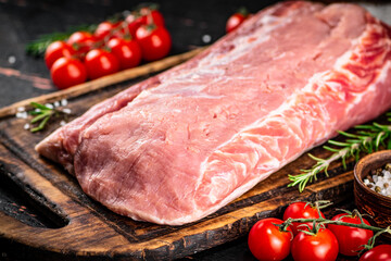 A piece of raw pork on a cutting board with tomatoes, spices and rosemary.