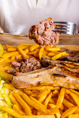 Cliente di un ristorante mentre regge con forchetta e coltello una salsiccia tagliata a metà di una grigliata di carne servita con contorno di patate fritte