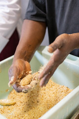 Aiutante chef mentre impana con le mani i crocchè di patate nel pangrattato pronti per essere fritti