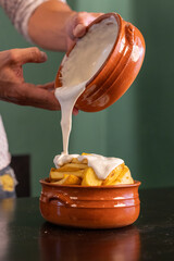 Formaggio fuso mentre viene versato su una porzione di patate fritte in un tegamino di terracotta...