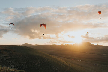 Paragliders flying under cloudy sky at sunset