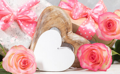 Gift boxes with pink polka dots bows, gentle peach color roses, empty white wooden heart. Close up.