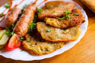 potato pancakes with fried sausages on a white plate