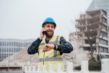 Smiling construction worker talking over smart phone standing by fence