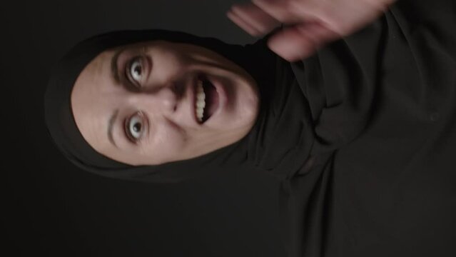 Vertical video of surprised excited female in hijab shocked with unbelievable offer isolated on black background. Amazed woman. Wow face