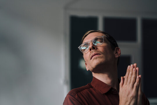 Businessman with eyes closed and hands clasped standing at office