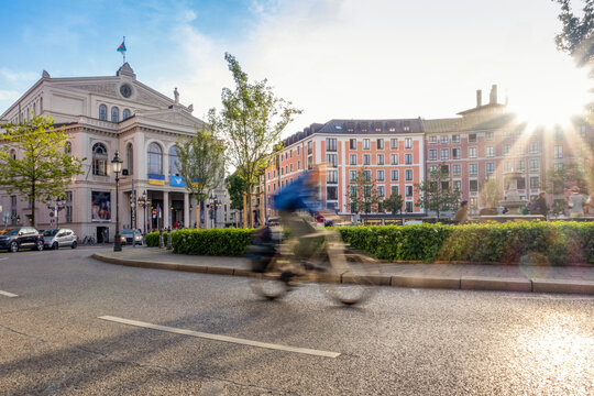 Germany, Bavaria, Munich, Blurred motion of cyclist passing through Gartnerplatz square at sunset