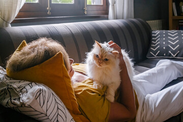 Senior woman with cat cuddling on sofa at home