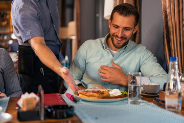 The waiter in the restaurant brings lunch to the whole family of three. Family launch concept.