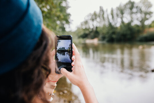 Woman clicking photos though smart phone by lake in park