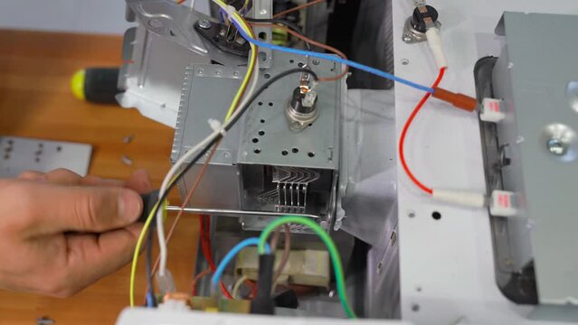 A man unscrews a screw with a screwdriver. He repairs the microwave oven. Close-up shot. magnetron.