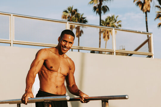 Smiling sportsman standing by parallel bars on sunny day