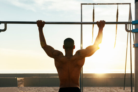 Sportsman exercising on gymnastics bar on sunny day