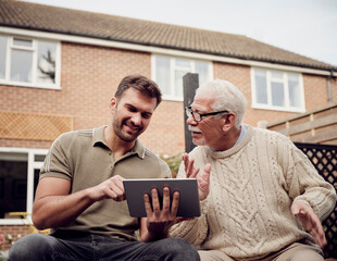 Father and son sitting in garden using digital tablet