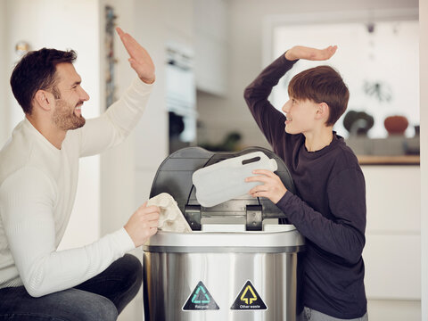 Father and son sorting waste paper and plastic into a sorting bin