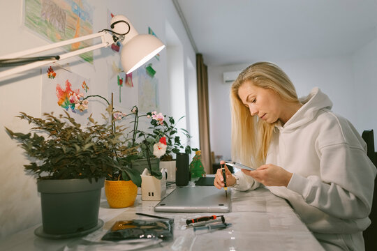 Woman using screwdriver disassembling laptop at home