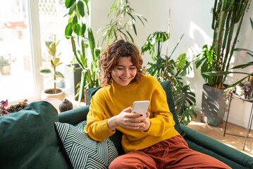 Smiling young woman using smart phone sitting on couch