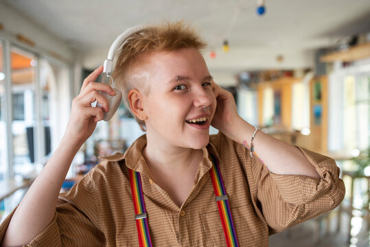 Happy non-binary person wearing headphones listening to music at cafe
