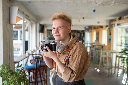 Smiling non-binary person holding camera taking pictures in cafe