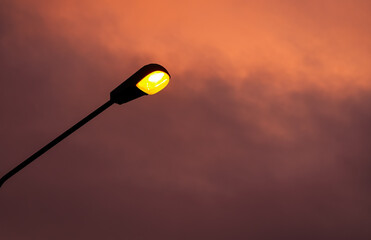 Public street lighting. One street warm light bulbs against amazing sunset sky background. Concept image for energy industry and rising electricity prices.