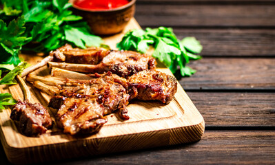 Grilled rack lamb on a cutting board with tomato sauce and parsley. 