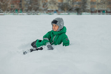 Fototapeta na wymiar the boy lies in the snow. the child plays in the snow. winter games in the fresh air. a boy in a green jumpsuit.
