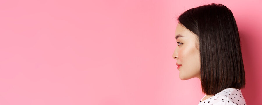 Beauty and skin care concept. Headshot profile of young beautiful asian woman with short dark hair, looking left at copy space, standing over pink background