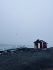 Small red fishing house at the sea coast, mist and fog background