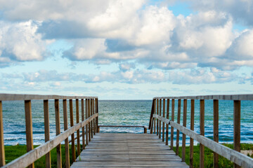 Fototapeta premium An empty wooden path with handrails for descending to a sandy beach. View of the calm sea and wooden gangway.