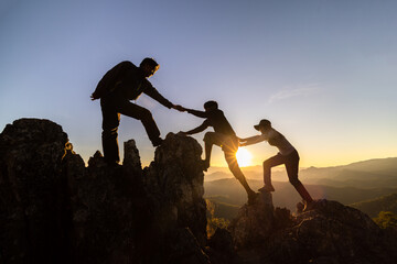 silhouette of Teamwork of three  hiker helping each other on top of mountain climbing team. Teamwork friendship hiking help each other trust assistance silhouette in mountains, sunrise. - obrazy, fototapety, plakaty