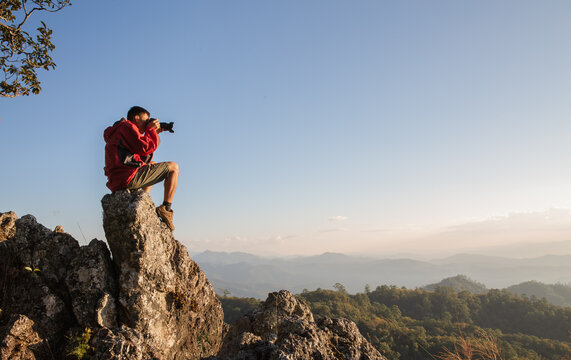 Man holding camera in his hands and making photos of the mountains during autumn morning,  Hiking and tourism concepts