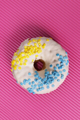 Fresh glazed donut with blue-yellow sprinkling in the colors of the flag of Ukraine on a pink background. Vertical Orientation