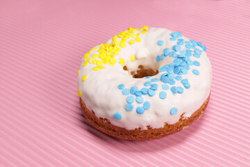 Fresh glazed donut with blue-yellow sprinkling in the colors of the flag of Ukraine on a pink background