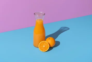 Keuken spatwand met foto Orange juice carafe and orange fruits isolated on a vibrant background © YesPhotographers