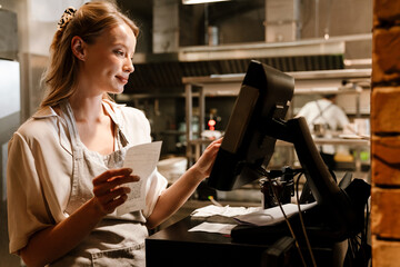 Young woman holding order receipts while working in restaurant kitchen